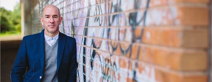 Jonathan Morgan, Partner at Zenko City Living, is pictured alongside a wall daubed with brightly coloured graffiti. letting agents